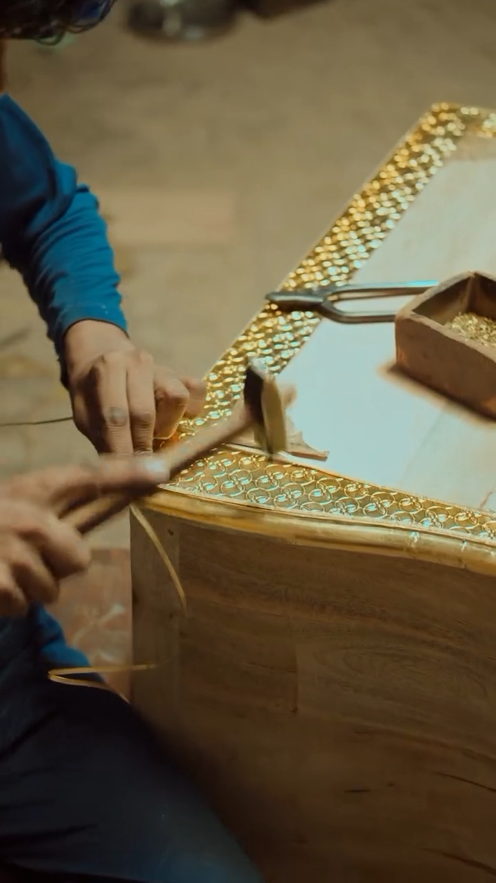 Craftsman hammering brass inlay onto a wooden piece